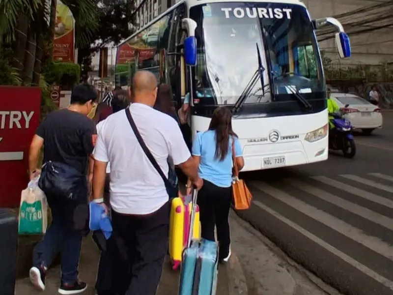 Travelers with luggage walking to a white tourist bus