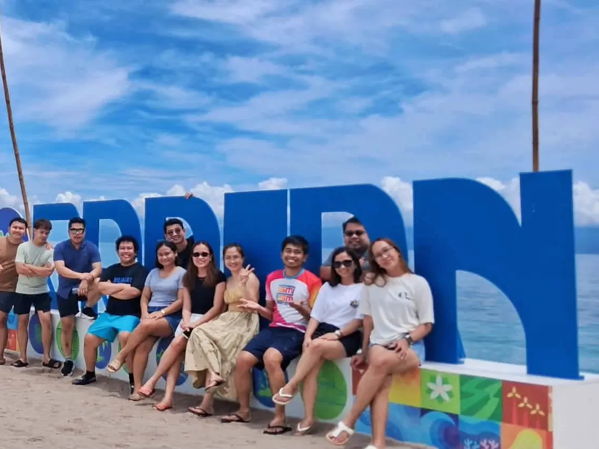 A group of Jushel guests sitting on a big Cebu sign by the sea, with a white van behind them